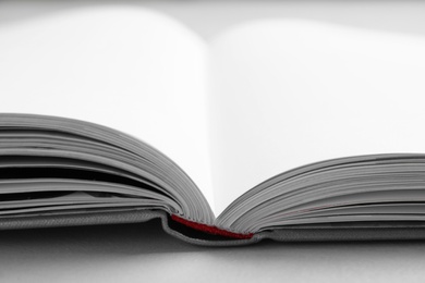 Photo of Open book with hard cover on light grey table, closeup