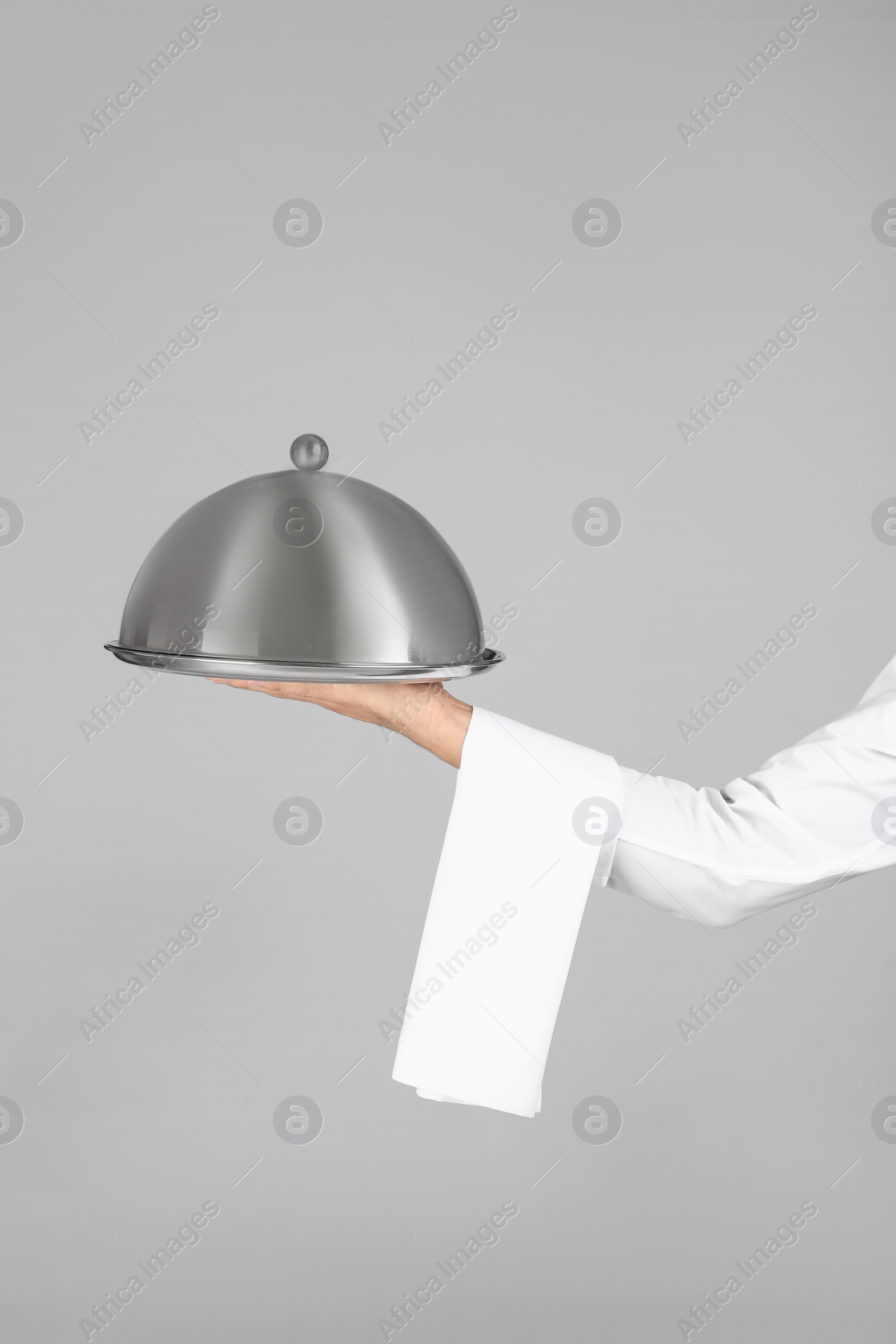 Photo of Waiter holding metal tray with lid on grey background