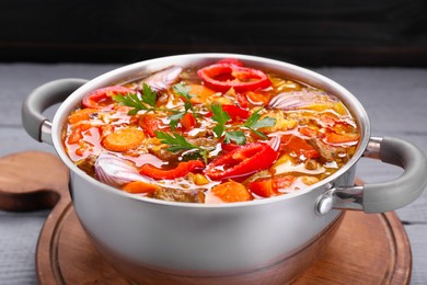 Photo of Saucepan of delicious vegetable soup with meat and ingredients on grey wooden table, closeup