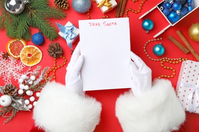 Photo of Santa Claus holding paper and Christmas decor on color background, top view