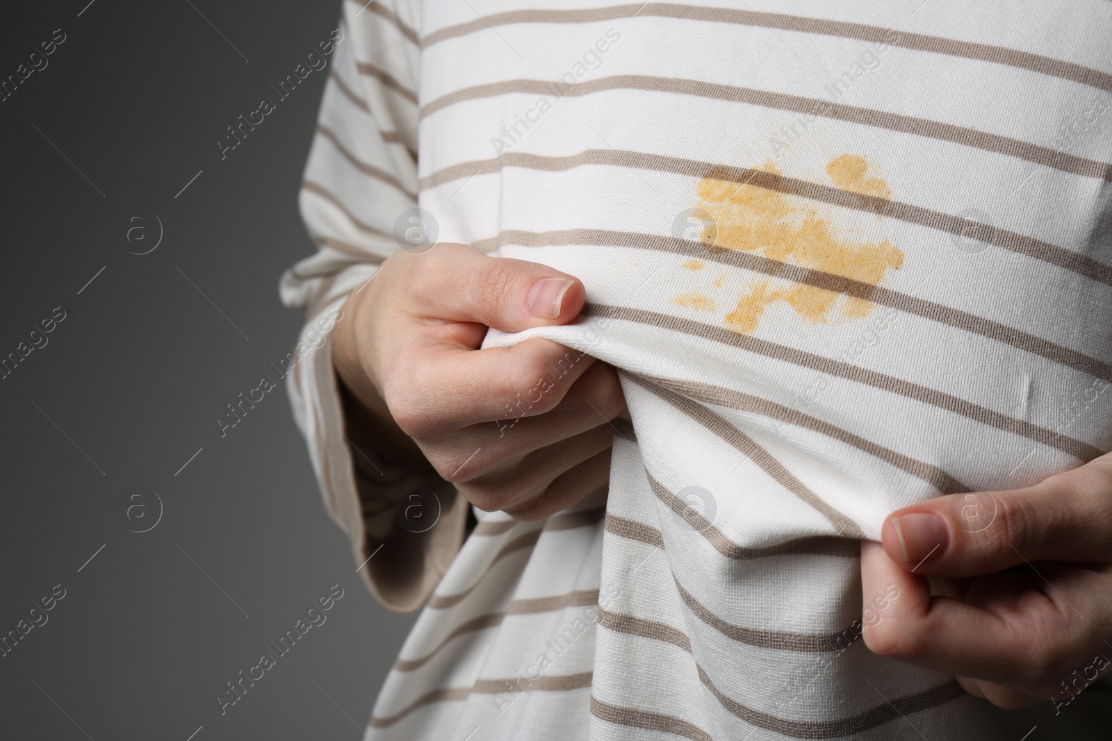 Photo of Woman showing shirt with yellow stain on grey background, closeup. Space for text