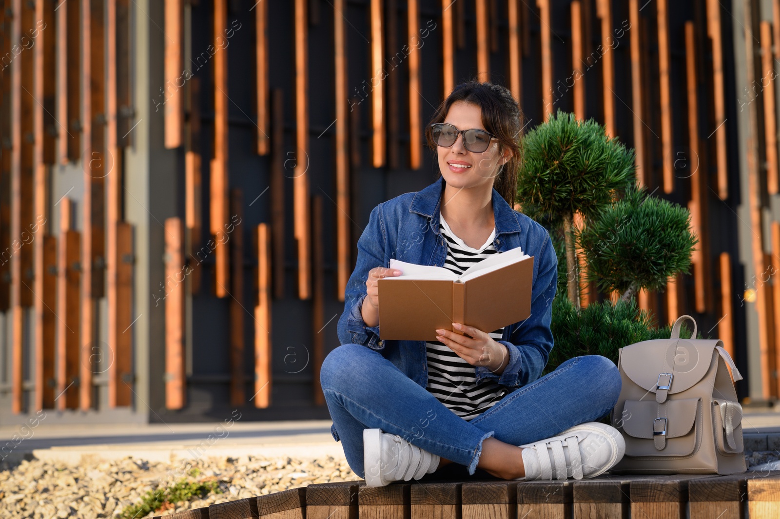 Photo of Young woman reading book on bench outdoors