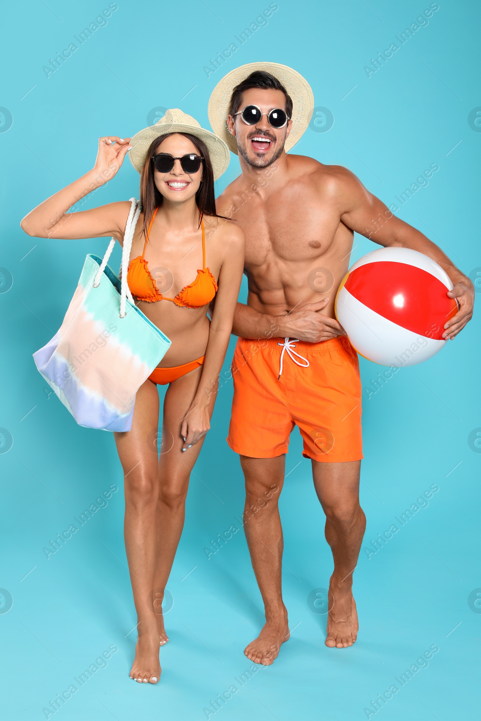 Photo of Young attractive couple in beachwear with ball and bag on blue background