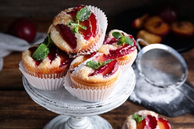 Photo of Delicious sweet cupcakes with plums on wooden stand, closeup
