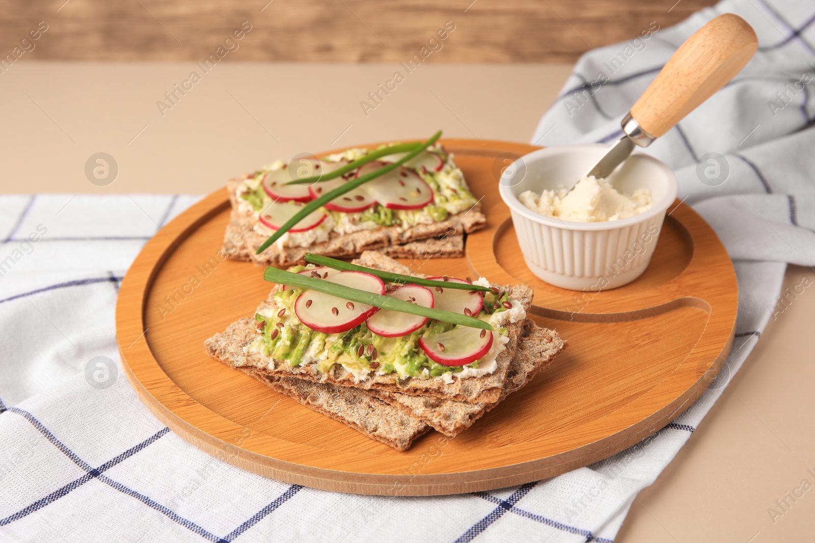 Photo of Fresh crunchy crispbreads with cream cheese, radish and green onion on beige table