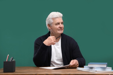 Portrait of senior teacher at table against green chalkboard