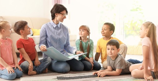 Image of Young woman reading book to little children indoors. Banner design