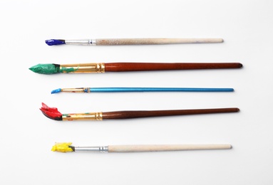 Brushes with colorful paints on white background, flat lay