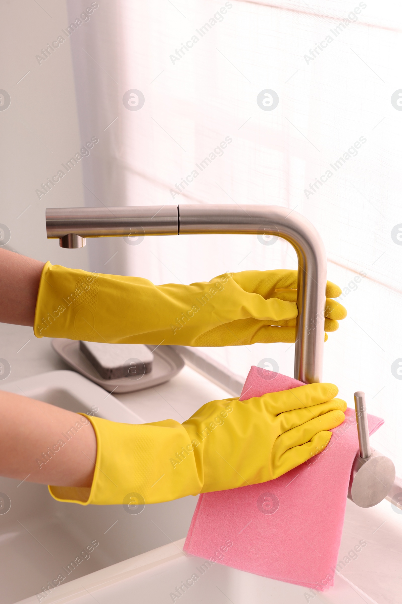 Photo of Woman in gloves cleaning faucet of kitchen sink with rag, closeup