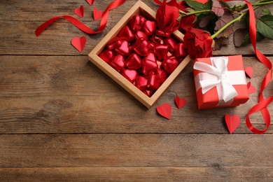 Heart shaped chocolate candies, bouquet and gift box on wooden table, flat lay. Space for text