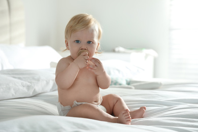 Cute little baby in diaper with pacifier sitting on bed at home