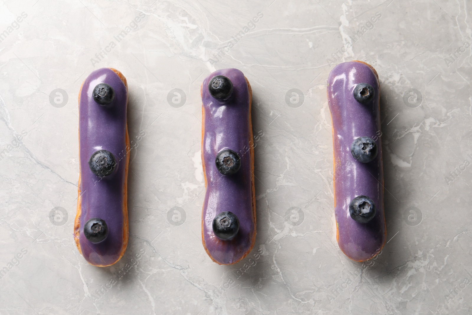 Photo of Tasty glazed eclairs with blueberries on grey marble table, flat lay