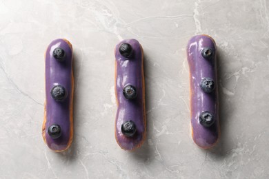 Photo of Tasty glazed eclairs with blueberries on grey marble table, flat lay