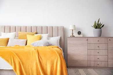 Photo of Stylish bedroom interior with soft yellow pillows and blanket