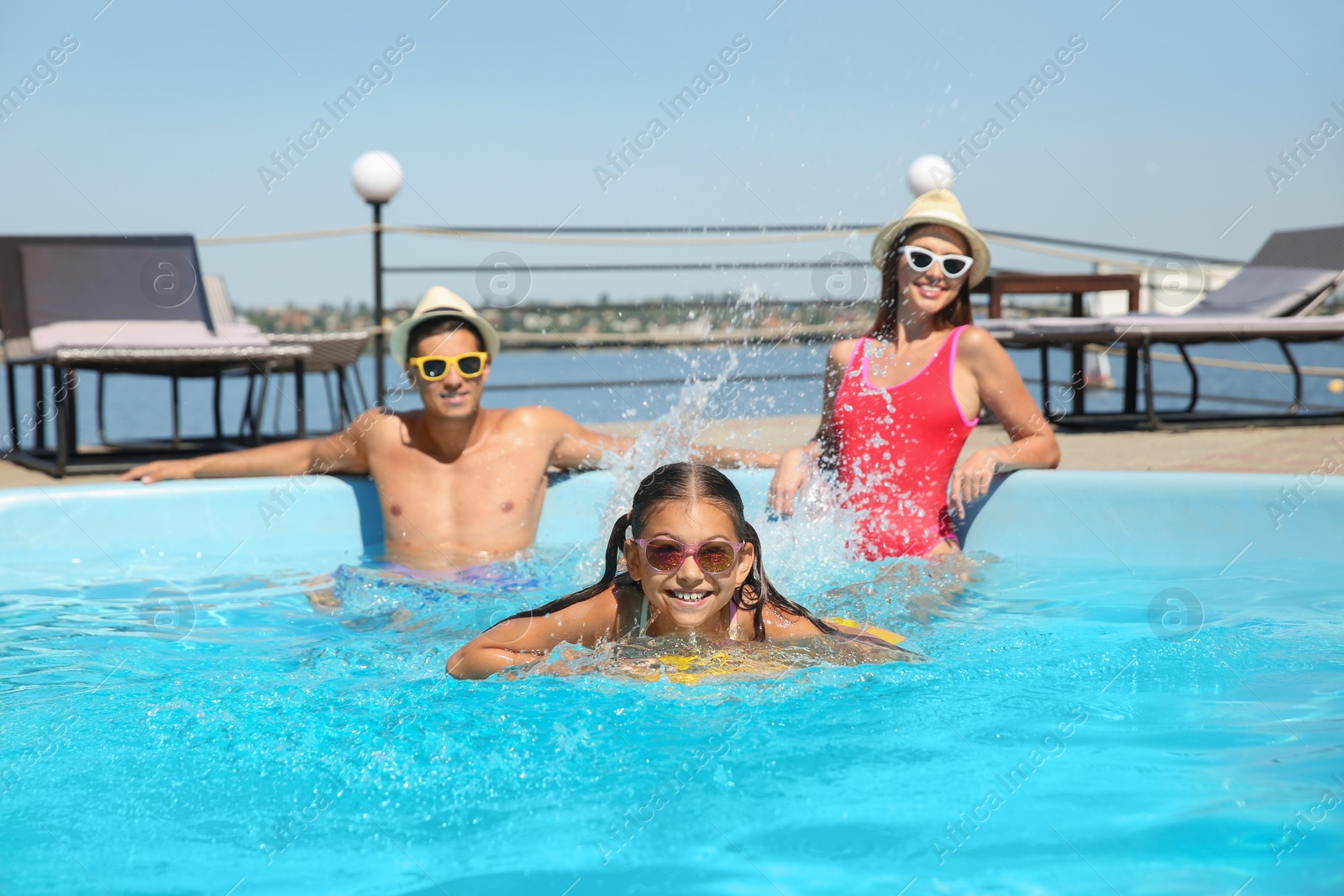 Photo of Happy girl and her parents having fun in swimming pool. Family vacation