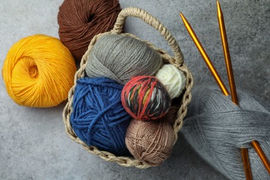 Soft woolen yarns and knitting needles on grey table, flat lay