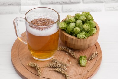 Photo of Mug with beer, fresh hops and ears of wheat on white wooden table