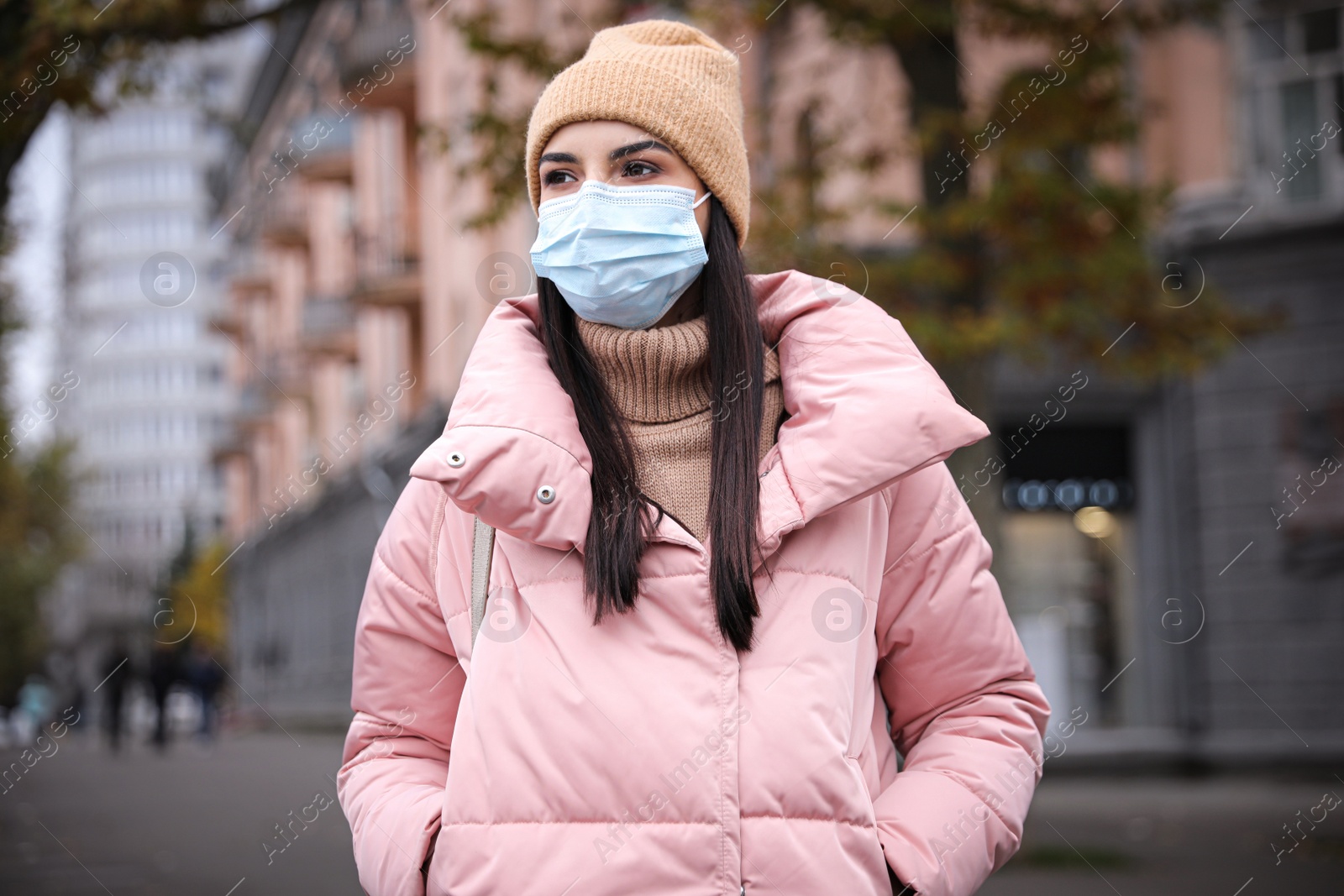 Photo of Young woman in medical face mask walking outdoors. Personal protection during COVID-19 pandemic