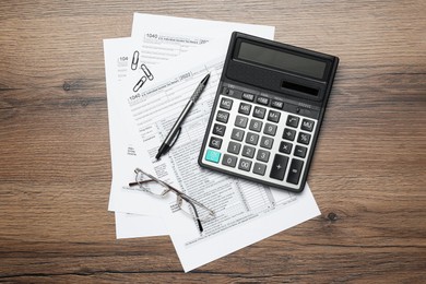 Photo of Calculator, glasses, documents and stationery on wooden table, flat lay. Tax accounting