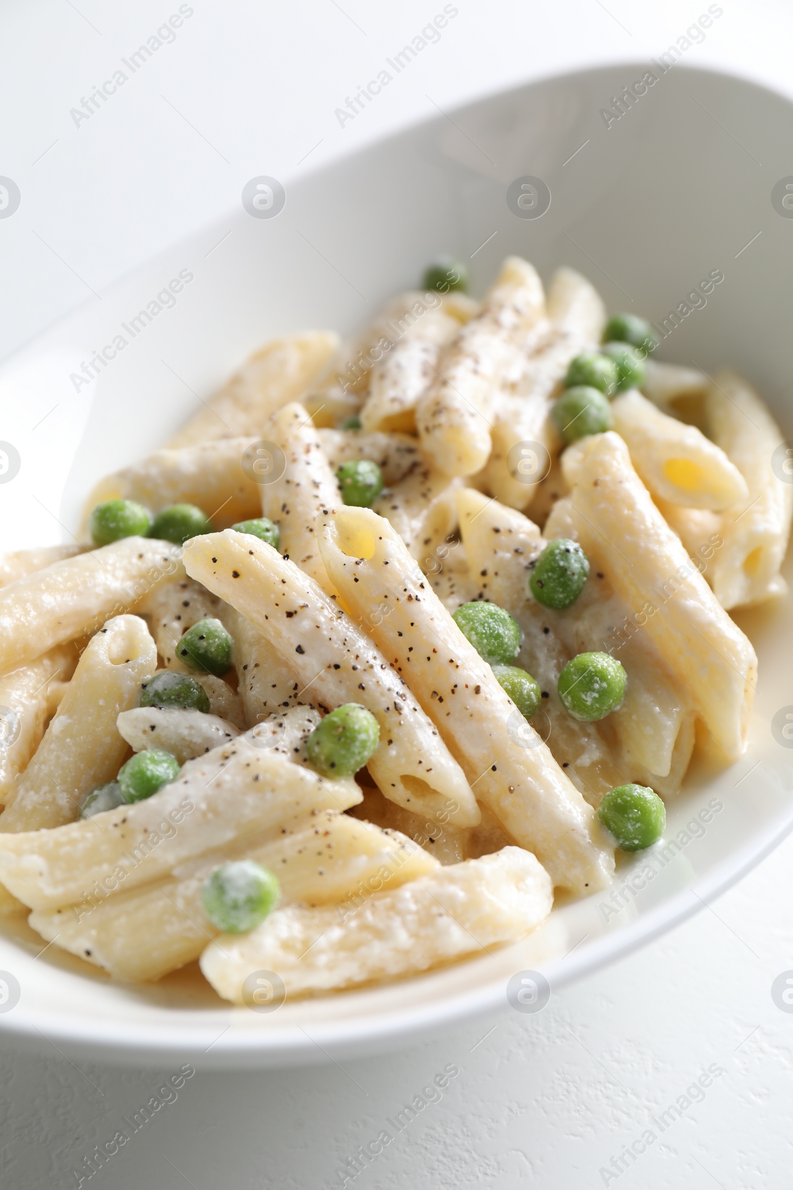 Photo of Delicious pasta with green peas and creamy sauce in bowl on white table