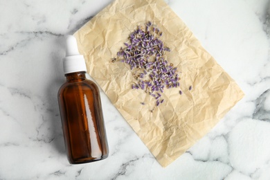 Photo of Natural herbal oil and lavender on marble background, top view