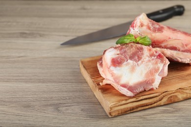 Photo of Cutting board with raw chopped meaty bones and basil on wooden table. Space for text