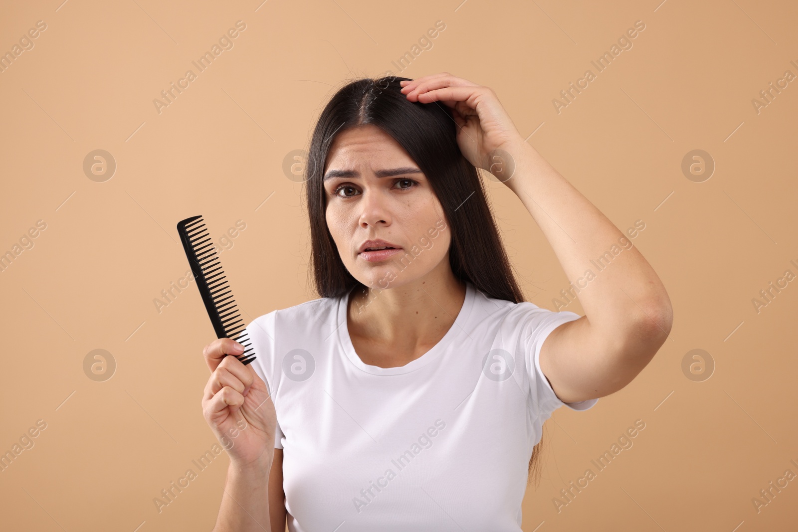 Photo of Emotional woman with comb examining her hair and scalp on beige background