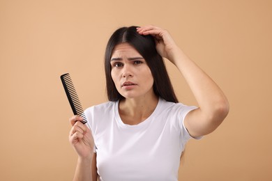 Photo of Emotional woman with comb examining her hair and scalp on beige background