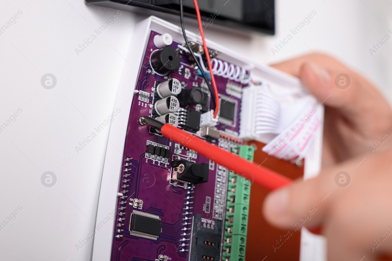 Photo of Man installing home security alarm system on white wall indoors, closeup