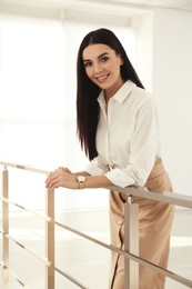 Happy young businesswoman leaning on railing in office