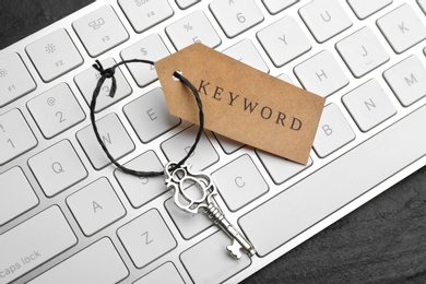 Photo of Keyboard, vintage key and tag with word KEYWORD on black table, closeup