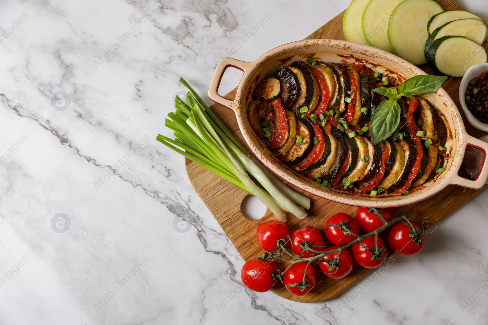 Photo of Delicious ratatouille and ingredients on white marble table, top view. Space for text