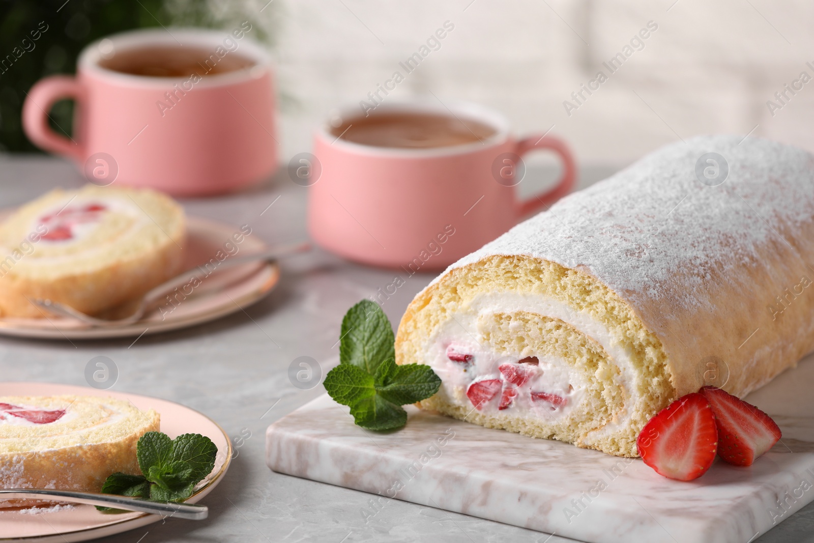 Photo of Delicious sponge cake roll with strawberries and cream on light grey table, space for text