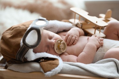 Cute newborn baby wearing aviator hat with toy sleeping in wooden crate