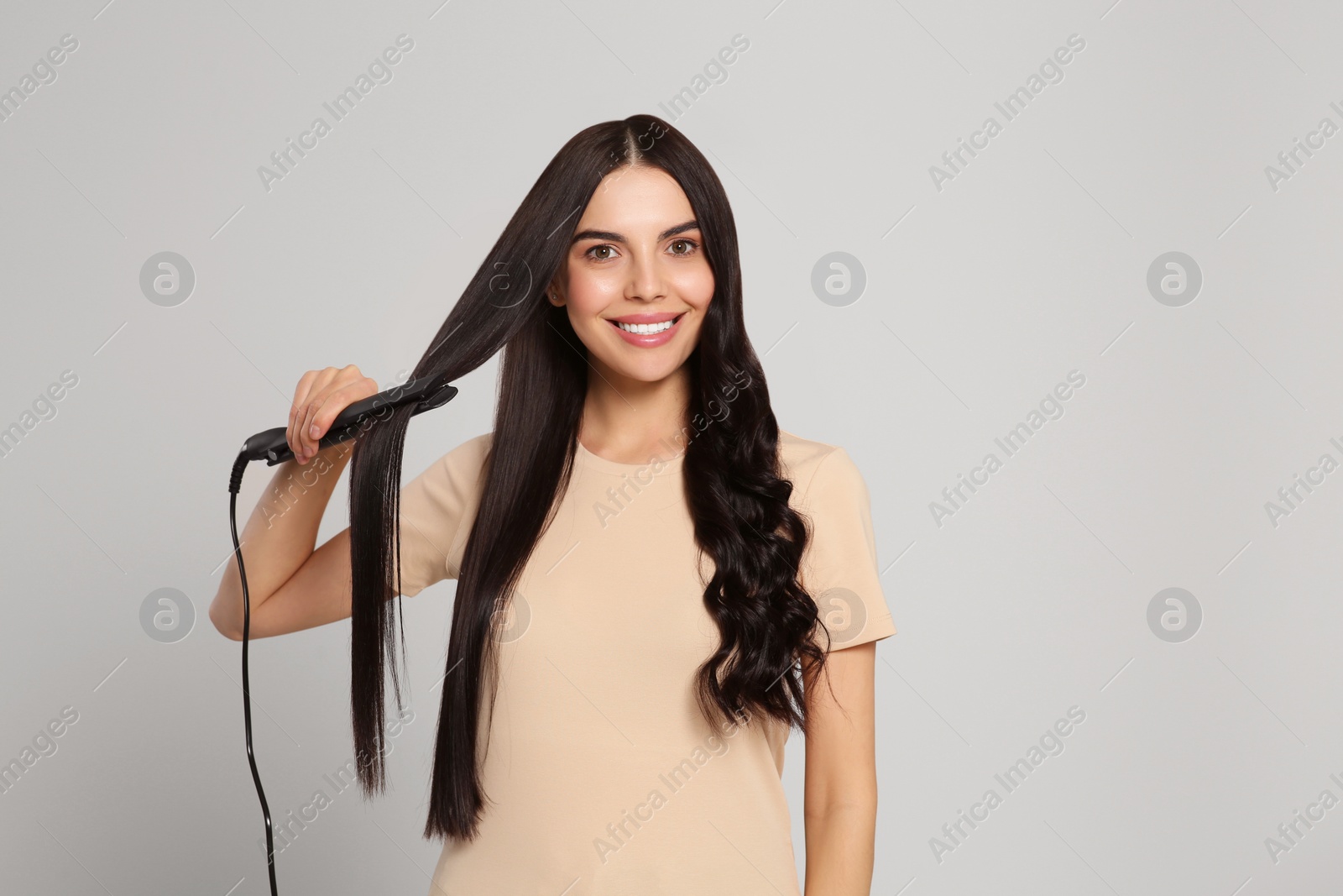 Photo of Beautiful happy woman using hair iron on light grey background. Space for text