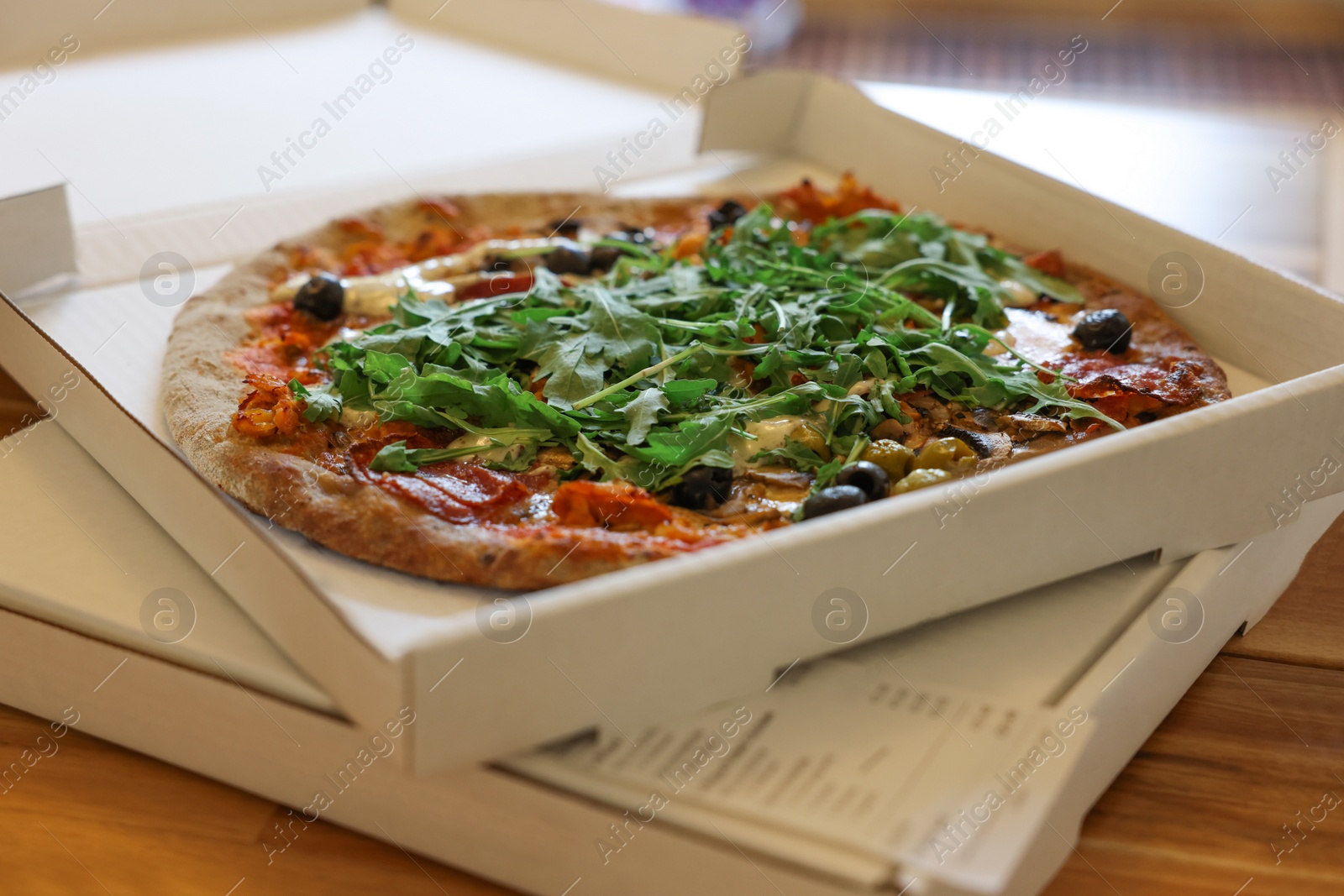 Photo of Delicious pizza with arugula, mushrooms and olives in box on wooden table, closeup