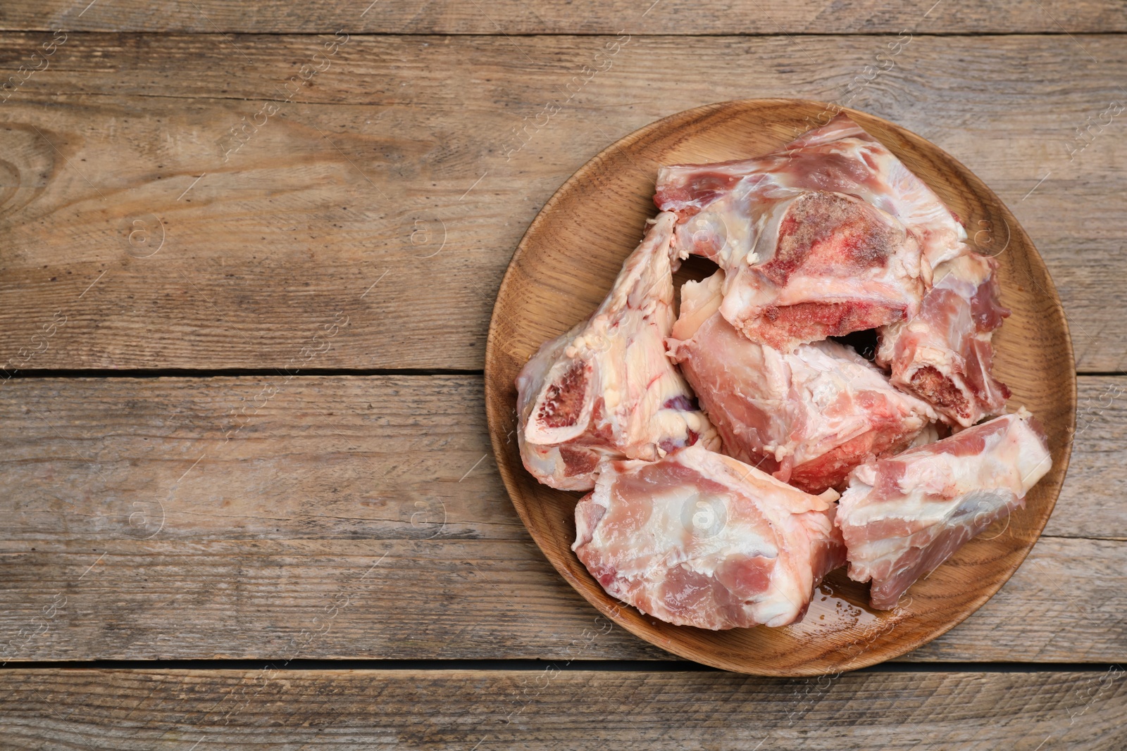 Photo of Plate with raw chopped meaty bones on wooden table, top view. Space for text