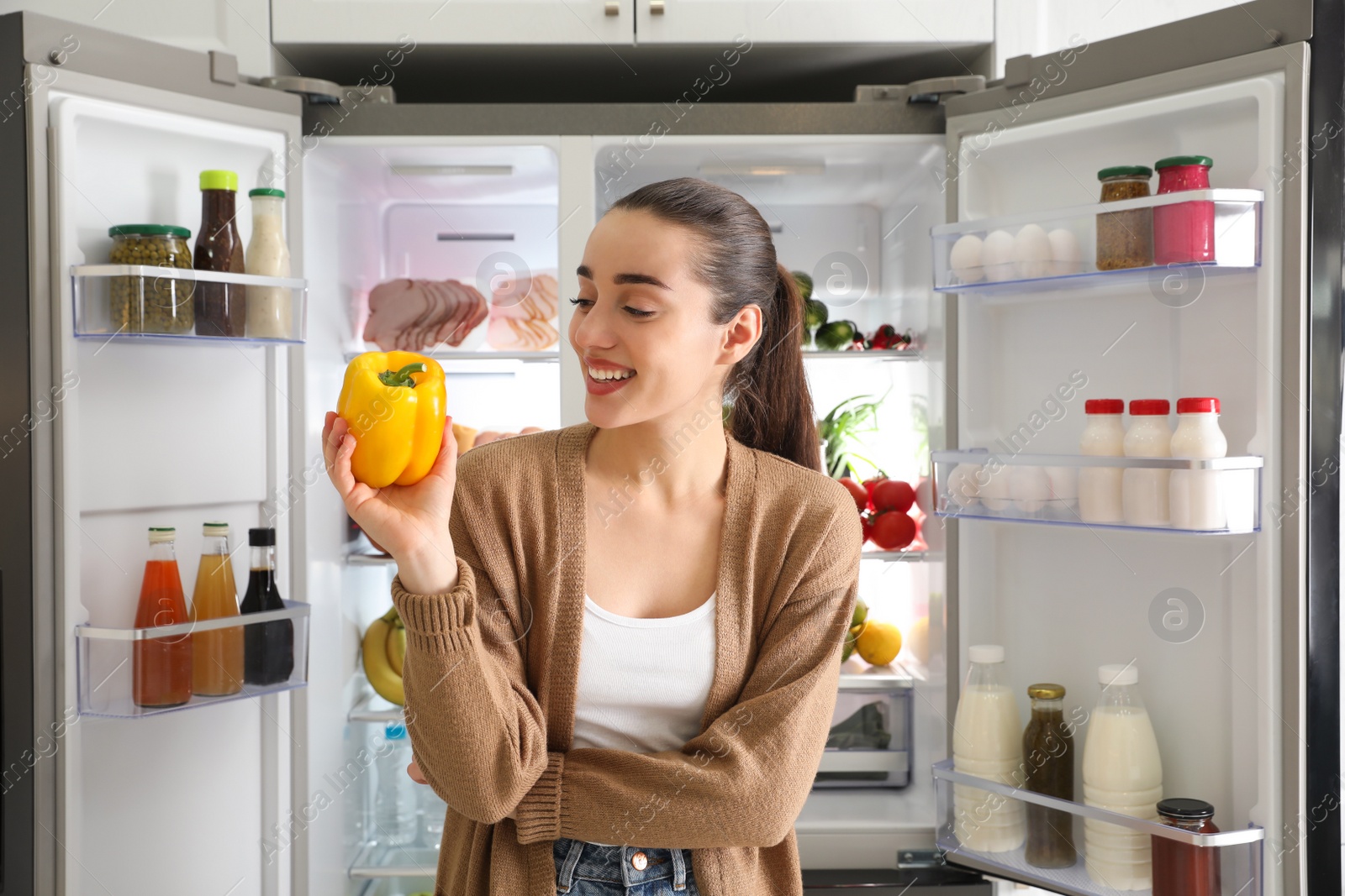 Photo of Young woman with bell pepper near open refrigerator