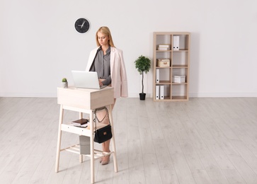 Young woman using laptop at stand up workplace indoors