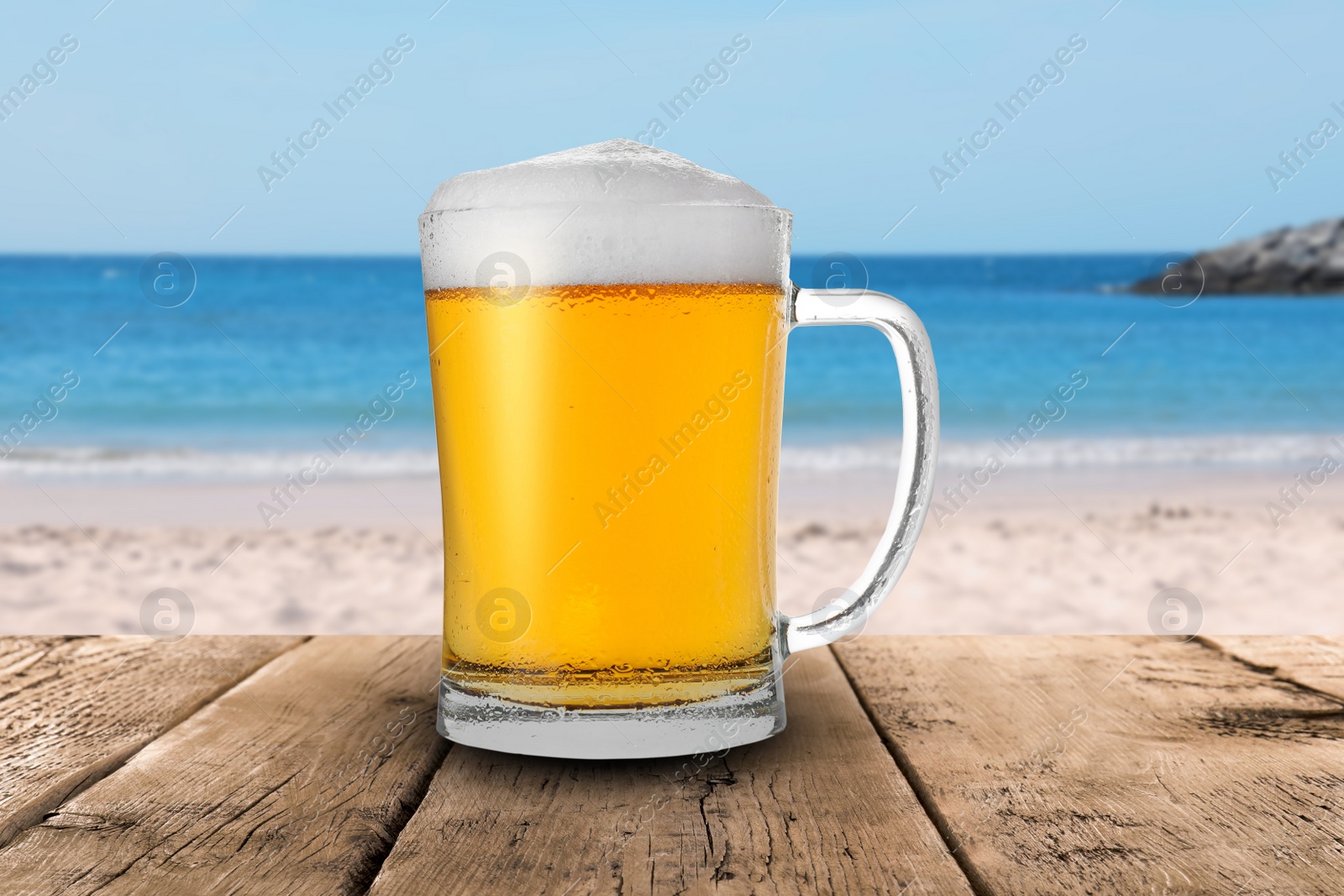 Image of Cold beer on wooden desk against blurred sea and sandy beach