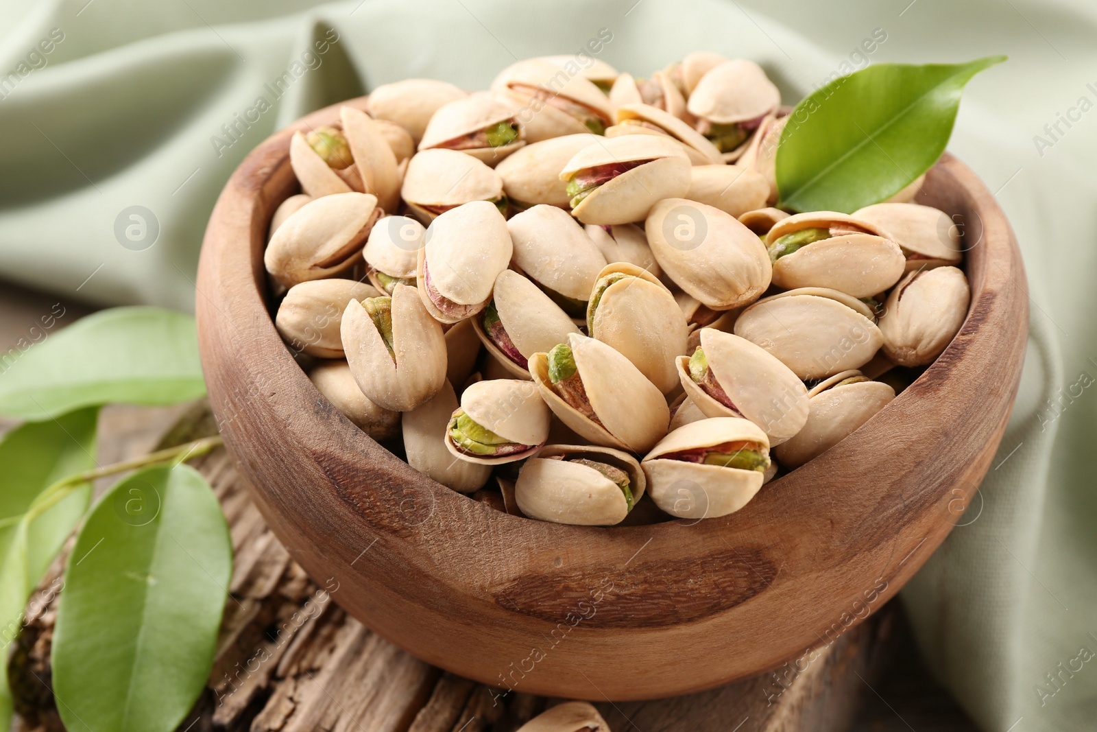 Photo of Delicious pistachios in bowl on wooden table, closeup