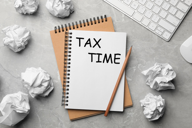 Image of Notebook with words TAX TIME and crumpled paper balls on grey table, flat lay