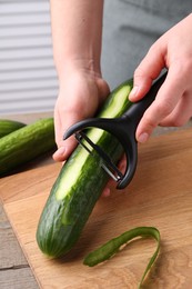 Woman peeling cucumber at wooden table indoors, closeup