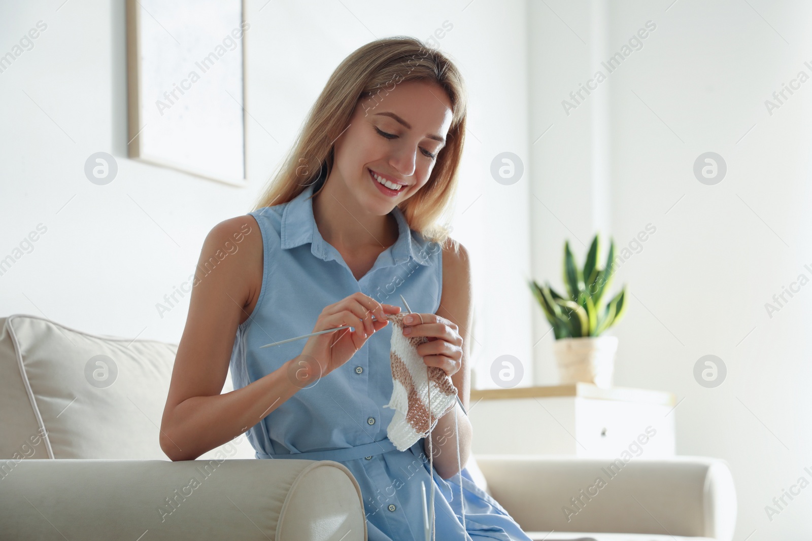 Photo of Young woman knitting with needles on sofa at home. Handicraft as hobby