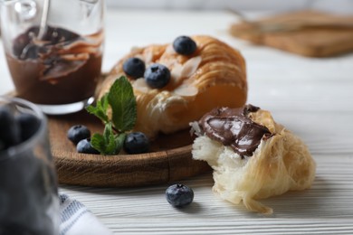 Photo of Delicious croissant with chocolate and blueberries on white wooden table, closeup