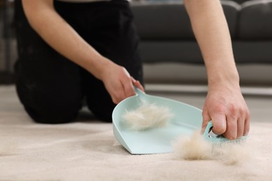 Photo of Man with brush and pan removing pet hair from carpet at home, closeup