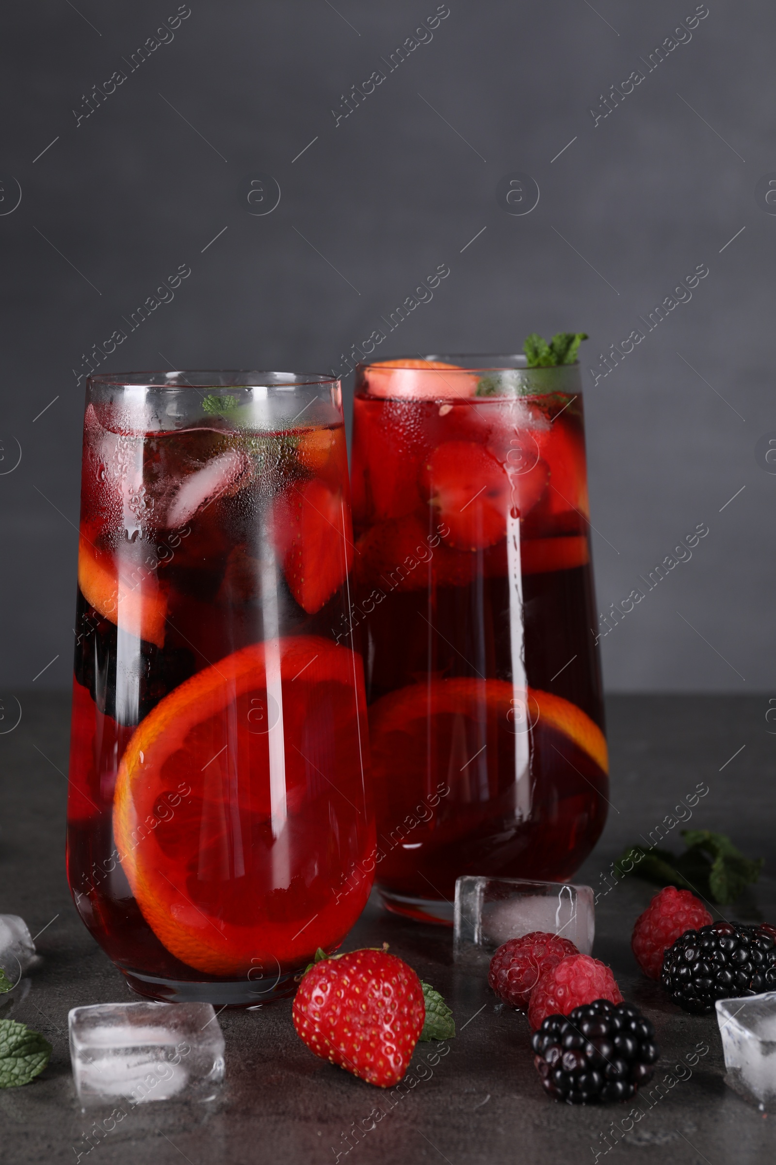 Photo of Delicious refreshing sangria, ice cubes and berries on grey table