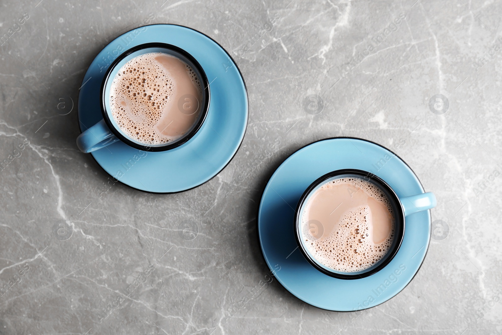 Photo of Cups with hot cocoa drink on grey table, top view