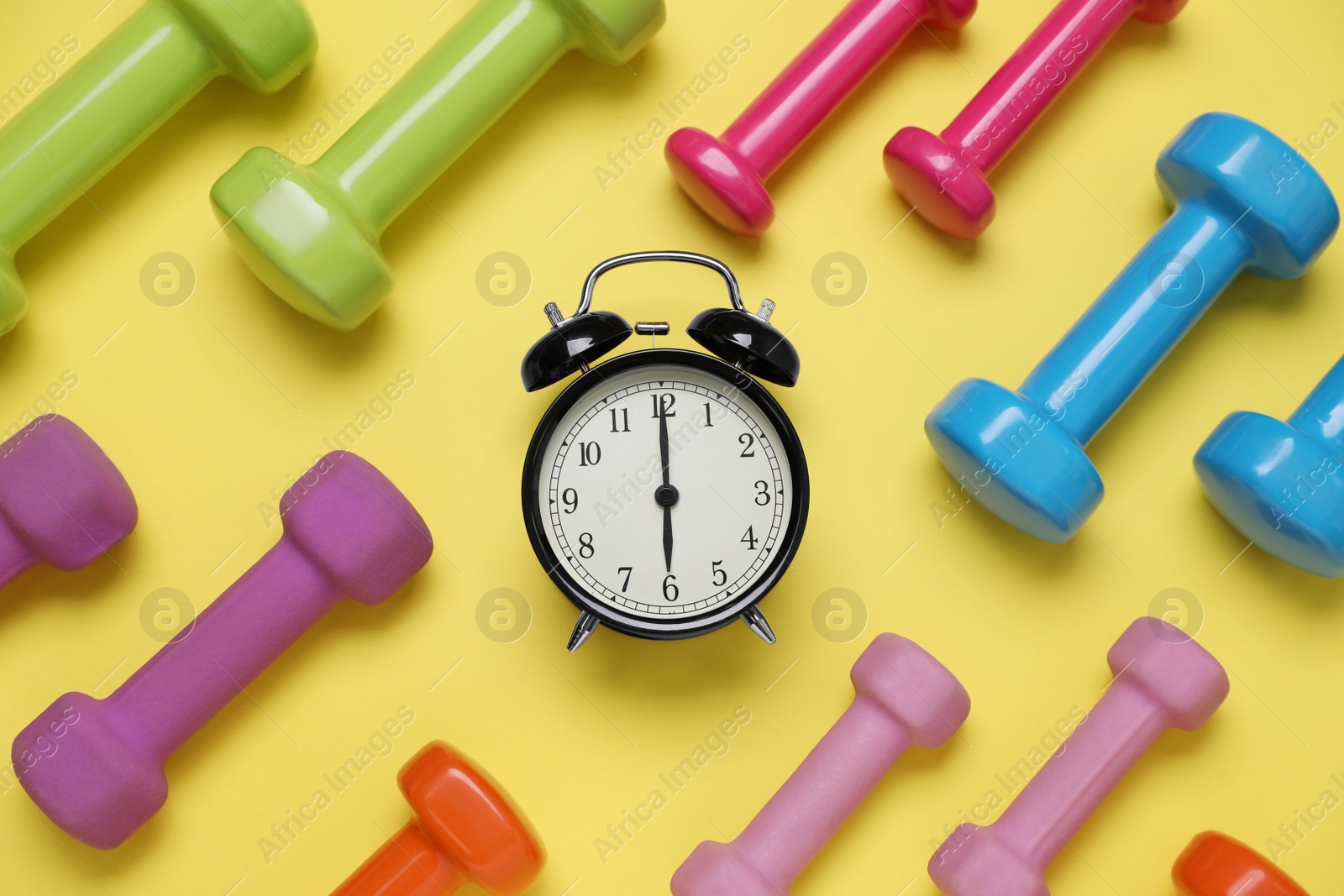 Photo of Alarm clock and dumbbells on yellow background, flat lay. Morning exercise