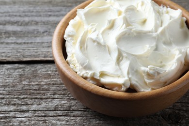 Photo of Bowl of tasty cream cheese on wooden table, closeup